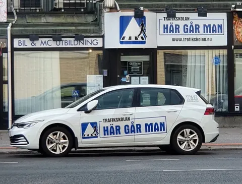 Trafikskolan Här Går Mans vita övningsbil parkerad utanför skolan