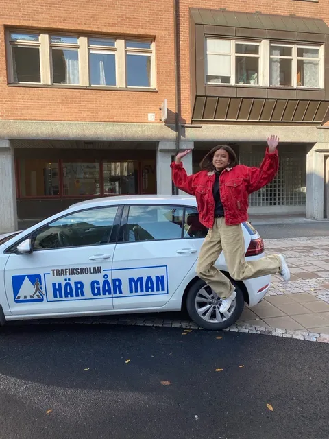 Glad körkortstagare hoppar av glädje bredvid övningsbilen