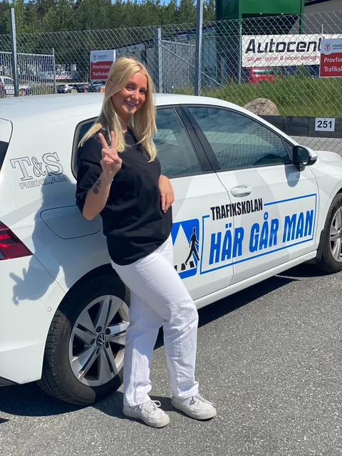 Elev firar godkänt körkort med segertecken vid övningsbilen